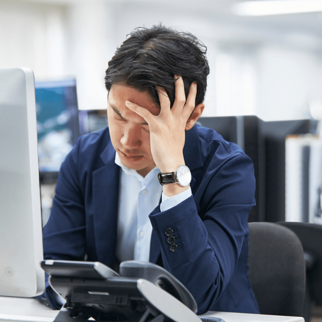 Tech downtime doesn’t just waste time, it drains productivity and frustrates your team. Frustrated office worker holding his head in front of a computer, overwhelmed by slow and inefficient technology at work.